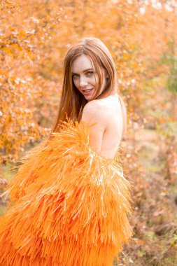 Kızıl saçlı genç kız bir sonbahar manzarasının arka planında poz veriyor.