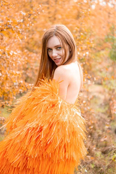 Kızıl saçlı genç kız bir sonbahar manzarasının arka planında poz veriyor.