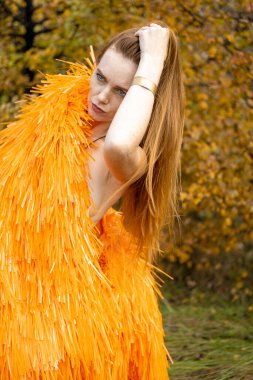 Kızıl saçlı genç kız bir sonbahar manzarasının arka planında poz veriyor.