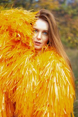 Kızıl saçlı genç kız bir sonbahar manzarasının arka planında poz veriyor.