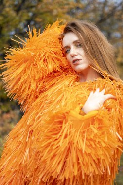 Kızıl saçlı genç kız bir sonbahar manzarasının arka planında poz veriyor.