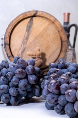 Ahşap bir fıçının arka planında bir demet üzüm ve cam bir sürahi.