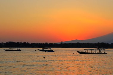 Endonezya 'nın tropikal bir adasında gün batımında siluetli teknelerle sahile.