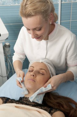 Kozmetik uzmanı kadın yüzüne pamuk pedi ya da süngerle dokunuyor. Kadın yalan söylüyor ve dinleniyor. Kozmetoloji yüz prosedürü.
