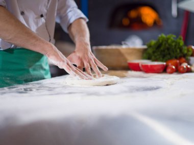 Şef pizza için hamur hazırlıyor. Elleri un serpiştirilmiş.