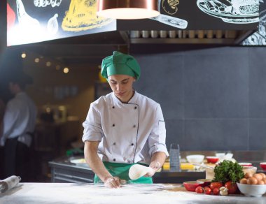 Şef elleri pizza için hamur hazırlarken masaya un serpiştirmiş.