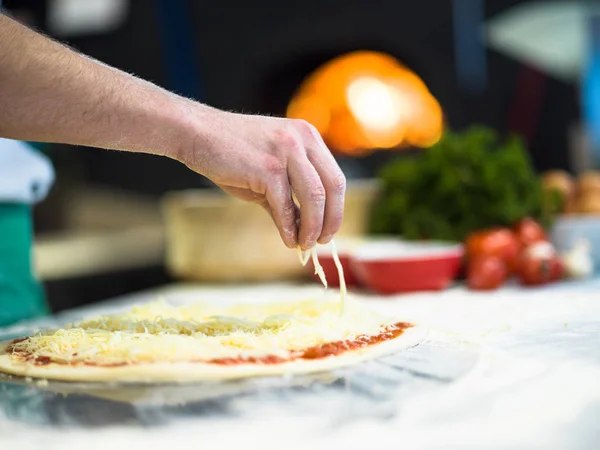 Chef Streut Käse Über Frischen Pizzateig Auf Küchentisch — Stockfoto