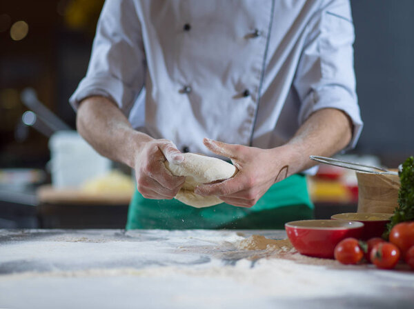 Chef hands preparing dough for pizza on table sprinkled with flour closeup
