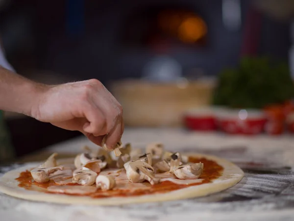 chef putting fresh mushrooms over pizza dough on kitchen table