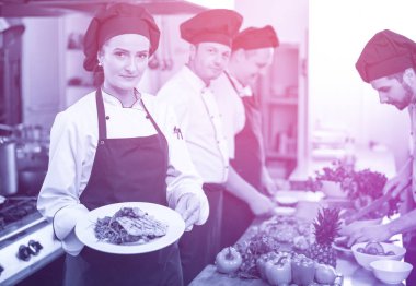 Şef, restoran mutfağında sebzeli kızarmış somon balığı filetosu tutuyor.