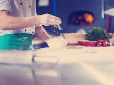 Şef elleri pizza için hamur hazırlarken masaya un serpiştirmiş.