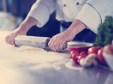 Şef pizza hamuru hazırlıyor. Üzerinde un tokası serpiştirilmiş.