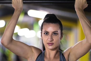 Genç kaslı kadın, Cross fitness eğitiminin bir parçası olarak yatay çubukta barfiks çekiyor.