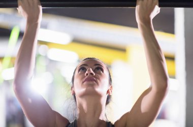 Genç kaslı kadın, Cross fitness eğitiminin bir parçası olarak yatay çubukta barfiks çekiyor.