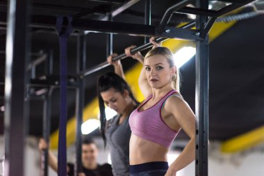 Bir grup genç kaslı sporcu, Cross fitness eğitiminin bir parçası olarak barfiks çekiyorlar.