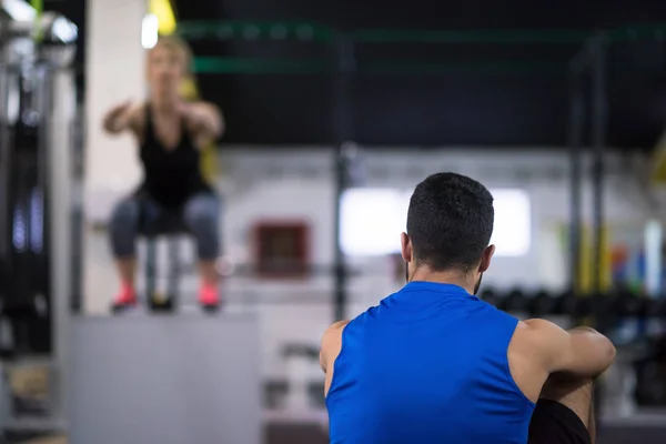 クロスフィットネスジムでフィットボックスに飛び乗るパーソナルトレーナーと若い運動選手の女性のトレーニング — ストック写真