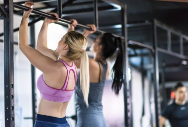 Bir grup genç kaslı sporcu, Cross fitness eğitiminin bir parçası olarak barfiks çekiyorlar.