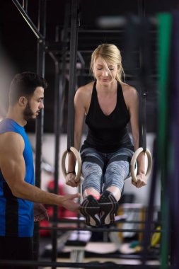 Genç atletik kadın spor salonunda jimnastik yüzükleri üzerinde kişisel antrenörle çalışıyor.