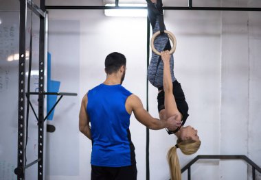 Genç atletik kadın spor salonunda jimnastik yüzükleri üzerinde kişisel antrenörle çalışıyor.