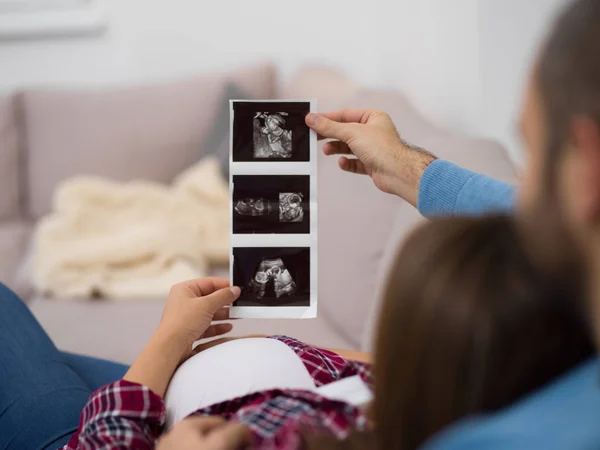 Mladí Těhotná Pár Hledá Ultrazvuk Foto Dítěte Při Odpočinku Pohovce — Stock fotografie