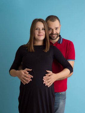 Mutlu genç bir çift hamile eşi karnı tutan adam portresi üzerinde mavi arka plan izole