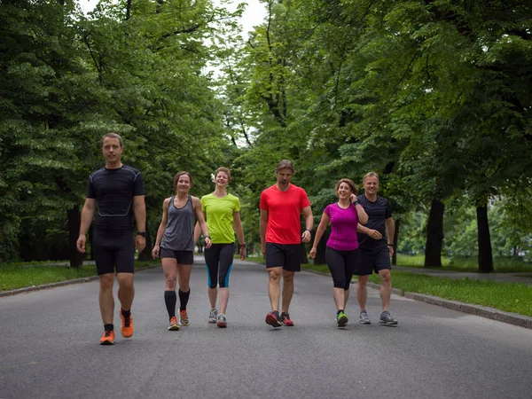 Bir grup sağlıklı insan şehir parkında koşuyor, koşucular sabah antrenmanında.