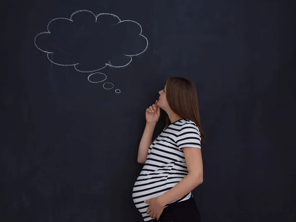 young pregnant woman thinking about names for her unborn baby to writing them on a black chalkboard