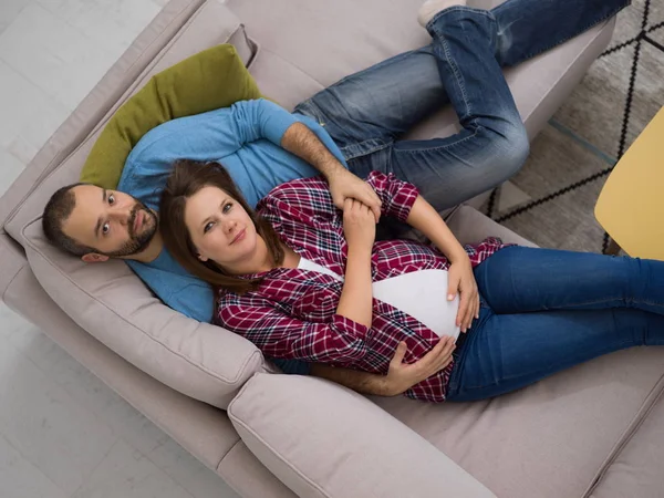 在家庭沙发沙发上放松的快乐怀孕夫妇的顶级视图 — 图库照片