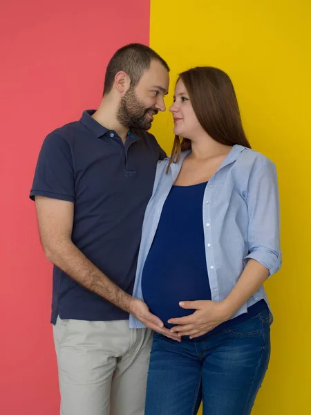一对幸福的年轻夫妇的肖像 男子抱着他怀孕的妻子腹部隔离在丰富多彩的背景 — 图库照片