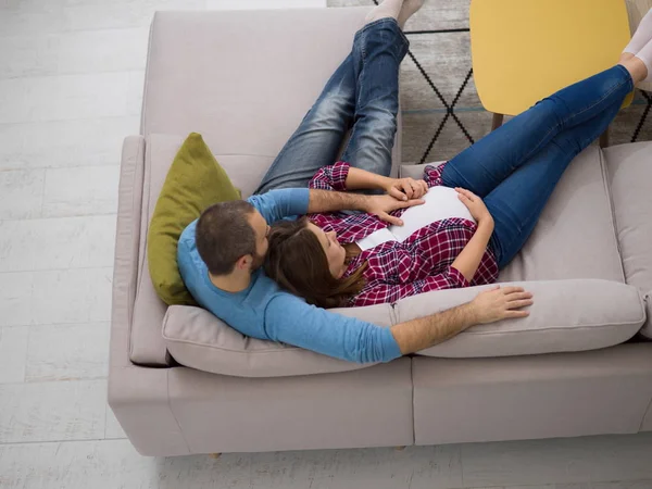 在家庭沙发沙发上放松的快乐怀孕夫妇的顶级视图 — 图库照片