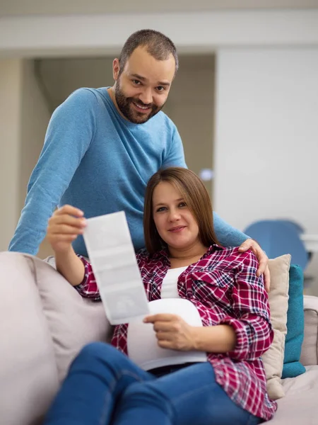 Genç hamile çift kanepede evde dinlenirken bebeğin ultrason fotoğraf arıyor