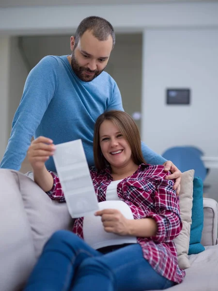 Genç hamile çift kanepede evde dinlenirken bebeğin ultrason fotoğraf arıyor