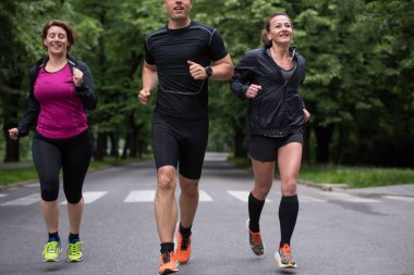 Bir grup sağlıklı insan şehir parkında koşuyor, koşucular sabah antrenmanında.