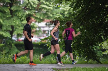 Bir grup sağlıklı insan şehir parkında koşuyor, koşucular sabah antrenmanında.