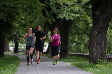 Bir grup sağlıklı insan şehir parkında koşuyor, koşucular sabah antrenmanında.
