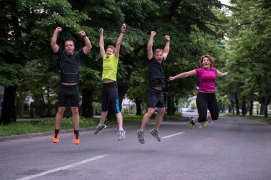 Bir grup sağlıklı koşucu sabah antrenmanı sırasında şehir parkında havaya atlıyor.