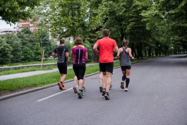 Bir grup sağlıklı insan şehir parkında koşuyor, koşucular sabah antrenmanında.