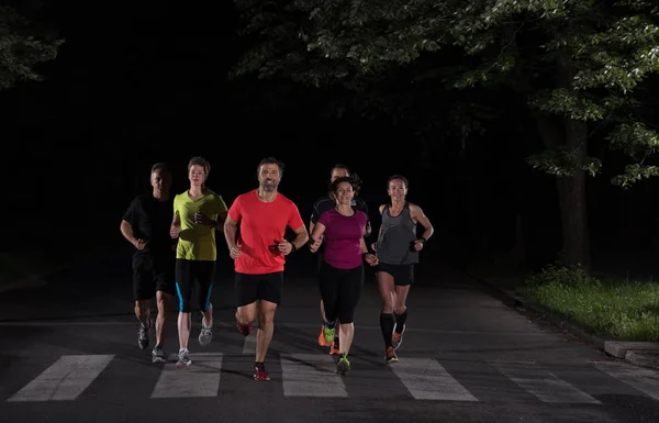 group of healthy people jogging in city park, runners team at night training