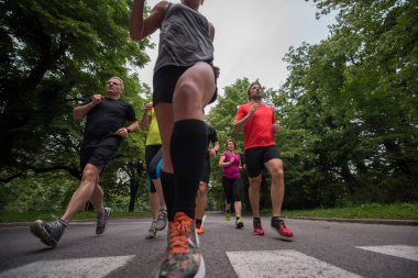 Bir grup sağlıklı insan şehir parkında koşuyor, koşucular sabah antrenmanında.