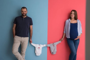 Güzel bir hamile kadın ve bebek bodysuits tutarak ve renkli arka plan üzerinde gülümseyen bekliyor bebek kocası