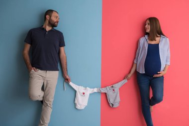 Güzel bir hamile kadın ve bebek bodysuits tutarak ve renkli arka plan üzerinde gülümseyen bekliyor bebek kocası
