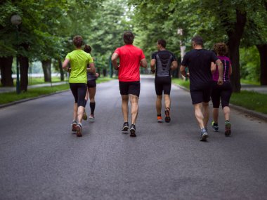 Bir grup sağlıklı insan şehir parkında koşuyor, koşucular sabah antrenmanında.