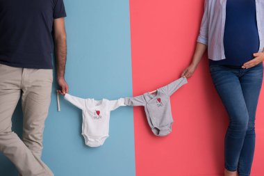 Güzel bir hamile kadın ve bebek bodysuits tutarak ve renkli arka plan üzerinde gülümseyen bekliyor bebek kocası