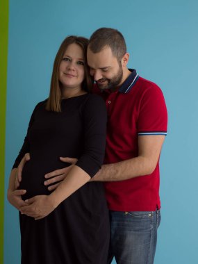 Mutlu genç bir çift hamile eşi karnı tutan adam portresi üzerinde mavi arka plan izole