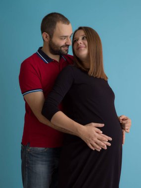 Mutlu genç bir çift hamile eşi karnı tutan adam portresi üzerinde mavi arka plan izole