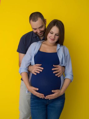 Mutlu genç bir çift hamile eşi karnı tutan adam portresi sarı arka plan üzerinde izole