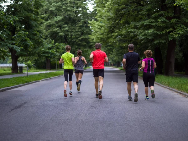Bir grup sağlıklı insan şehir parkında koşuyor, koşucular sabah antrenmanında.
