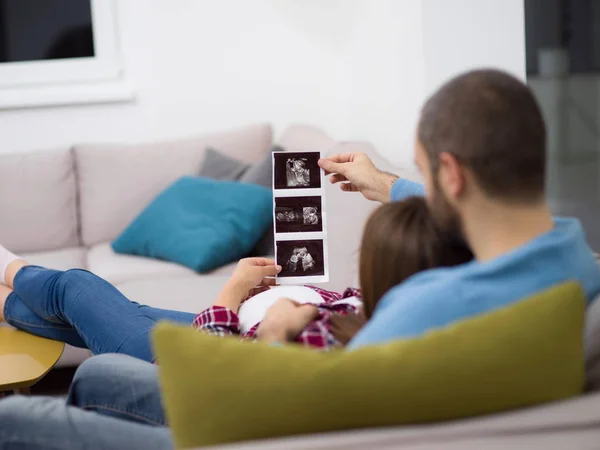 Genç Hamile Çift Kanepede Evde Dinlenirken Bebeğin Ultrason Fotoğraf Arıyor — Stok fotoğraf