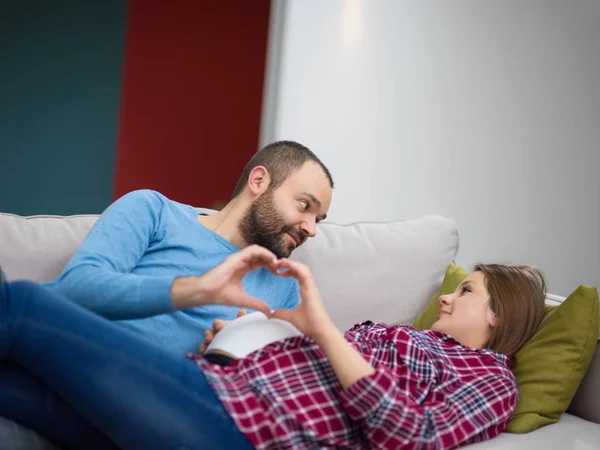 自宅のソファでリラックスしながら指で幸せな男と妊娠中の女性の心を示す署名します — ストック写真