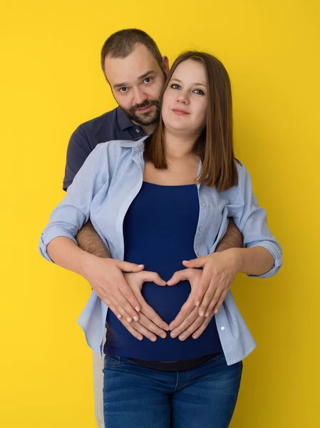 幸せな若いカップル 彼の妊娠した妻の腹を抱きかかえたの肖像画は 黄色の背景の上分離 — ストック写真